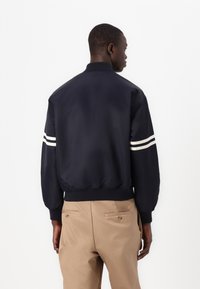 Chaqueta bomber de la marina hecha de tejido suave, con rayas blancas en las mangas, puños y dobladillo acanalados, y un diseño minimalista.