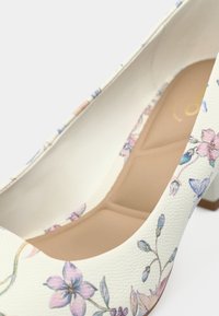 Escarpin blanc à talon haut avec imprimé floral aux couleurs pastel, matériau synthétique texturé, et semelle beige avec un coussin subtil.