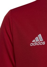 Maglietta sportiva rossa con collo a giro e il logo Adidas ricamato in bianco sulla parte superiore sinistra. Tessuto liscio e strutturato.