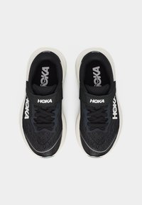 Ζευγάρι μαύρα και λευκά παπούτσια τρεξίματος Hoka με κορδόνια και ιμάντες Velcro, φωτογραφημένα από πάνω σε λευκό φόντο.