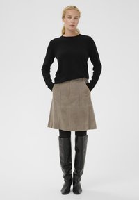 Schwarzer figurbetonter Pullover, hellbrauner Wildlederrock mit vertikalen Nähten und lange schwarze Lederstiefel. Einfaches, strukturiertes Design mit Taschen.