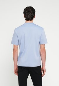 Svetlomodré tričko s krátkym rukávom z jemnej látky, s okrúhlym výstrihom a voľným strihom, v kombinácii s čiernymi nohavicami.