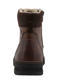 Botín de cuero marrón hasta el tobillo con forro de piel sintética, forma redondeada y cremallera lateral. Presenta una suela de goma con el logo "TOM TAILOR" grabado.