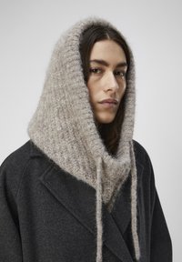 Textuurvolle grijze sjaapkap van zacht, grof gebreid materiaal, gecombineerd met een donkere wollen jas met reverskraag en dubbelgeknoopt ontwerp.