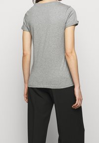 Camiseta gris de manga corta con puños enrollados, textura suave, forma ajustada y un cuello redondo sencillo, combinada con pantalones negros de corte ancho.