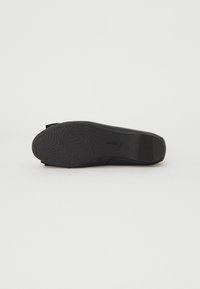 Zwarte schoen met een platte rubberen zool, voorzien van een golvend profielpatroon, een glad design en een instapstijl zonder zichtbare bevestigingsmiddelen.