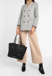 Gray plaid double-breasted blazer, beige wide-leg pants, black leather tote with gold accents, and glossy black ankle boots.