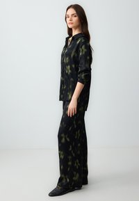 Zwart en groen abstract bedrukte zijden shirt en broekset. Loose fit, lange mouwen en notch-kraag. Gladde textuur en minimale details.