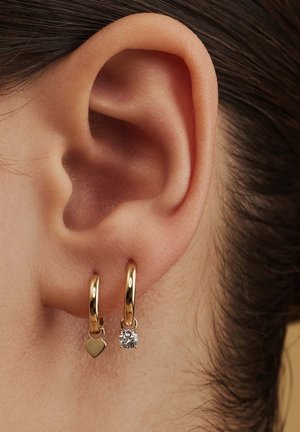 Goldene Creolen mit einem herzförmigen Anhänger und einem klaren Steinpendant. Das Design ist schlank, mit einer glänzenden Oberfläche, die am Ohrläppchen hängt.