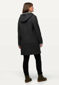 Cappotto in misto lana grigio scuro con cappuccio, dotato di un morbido rivestimento grigio chiaro, design moderno e lunghezza a metà coscia. Pantaloni neri e stivali.