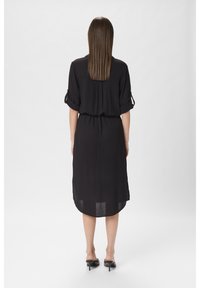 Abito nero con una vestibilità rilassata, maniche corte arrotolate, texture morbida, lunghezza al ginocchio e orlo leggermente curvato sul retro.