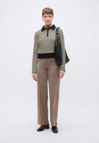 Camisola de malha às riscas com gola preta, combinada com calças largas bege elegantes e uma mala de ombro preta texturada. Botins pretos até ao tornozelo.