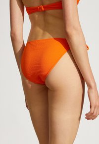 Ljusorange bikiniunderdel med en strukturerad tygkvalitet, hög midja design och rullad midjebanddetalj. Slät yta mot huden.