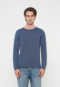 Koszulka z długim rękawem i okrągłym dekoltem, wykonana z teksturowanej, ciemnoniebieskiej tkaniny. Charakteryzuje się dopasowanym krojem i bezszwowymi ramionami. Noszona z jasnoniebieskimi dżinsami.