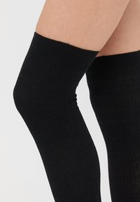 Čierne ponožky po kolená vyrobené z rebrovanej tkaniny, s hladkým povrchom a tesným strihom okolo vrchu.