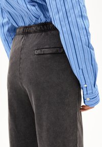 Donkergrijze broek van zacht, textuurstof met een elastische tailleband, gecombineerd met een blauw gestreept overhemd met knopen.