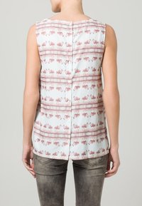 Top sans manches en tissu blanc orné d'un motif de flamants roses et de fines lignes horizontales. Détail à boutons au dos.