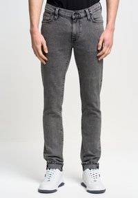 Jeans gris de corte slim con un acabado texturizado. Presenta cinco bolsillos, un cierre de botón y un lazo negro para el cinturón. Combinados con zapatillas blancas.