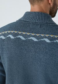 Sötét kék kötött pulóver bordás gallérral és világoskék, valamint sárga mintázattal a háton. Sima textúra.