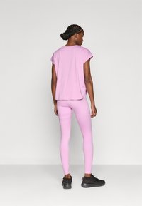 Ροζ κοντομάνικη μπλούζα με χαλαρή εφαρμογή, συνδυασμένη με ροζ κολάν με υφή, και μαύρα αθλητικά παπούτσια.