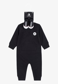 Svart bomullsbyxdress med långa ärmar, framfickor och v-ringning. Inkluderar avtagbara mini svarta sneakers med vita sulor.