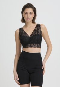 Bralette en dentelle noire avec bretelles larges et festonnées ainsi qu'un design court. Comprend des motifs floraux complexes et un tissu lisse et extensible.