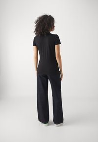 Svart kortärmad t-shirt med en smal silhuett, kombinerad med vida, mörka jeans och vita sneakers mot en neutral bakgrund.