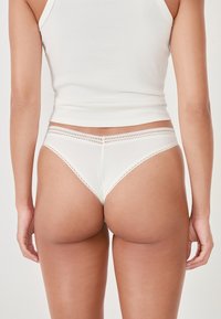Tanga bianco a costine con delicato pizzo, caratterizzato da una texture morbida e una copertura minima. La vita è liscia e discreta.
