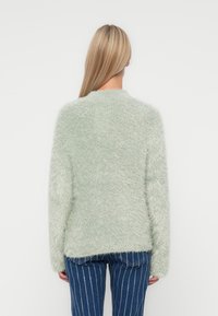 Hellgrüner, flauschiger Pullover mit langen Ärmeln und rundem Ausschnitt, der eine weiche Textur und eine lockere Passform im Rückenbereich aufweist.