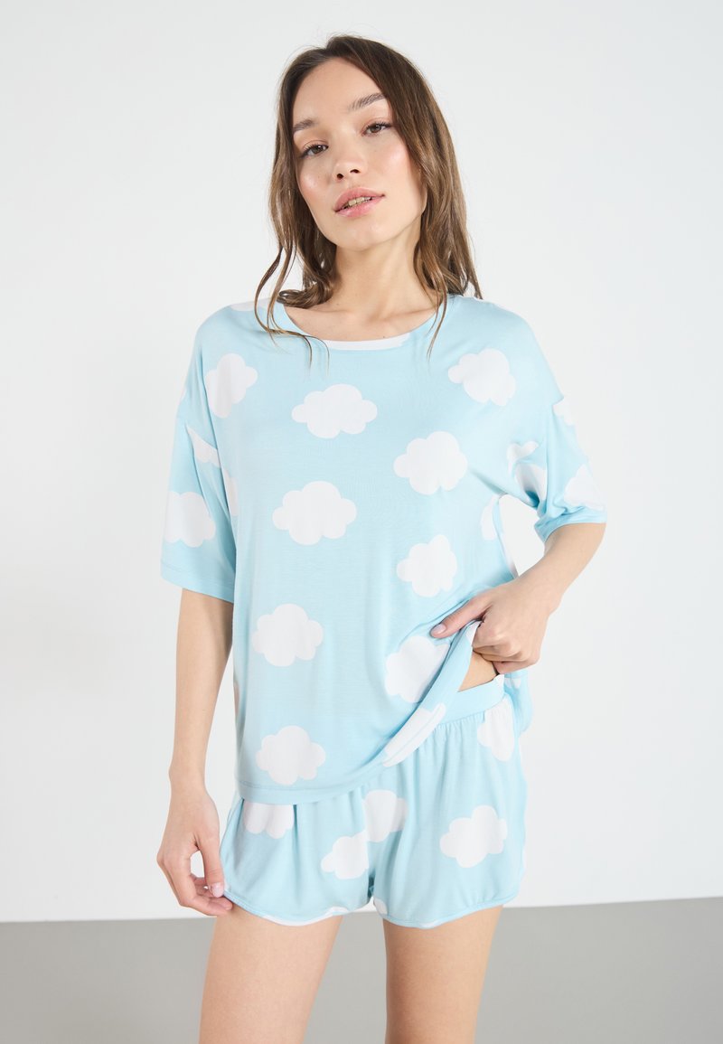 Set de lounge bleu deschis, format dintr-un tricou lejer și pantaloni scurți, ambele decorate cu modele de nori albi. Material moale, elastic, cu croială lejeră.