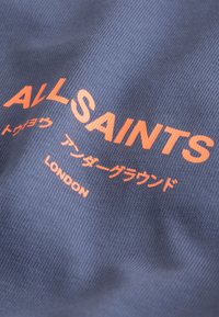 Tela azul con texto naranja que dice "ALL SAINTS", caracteres japoneses y "LONDON" impreso.