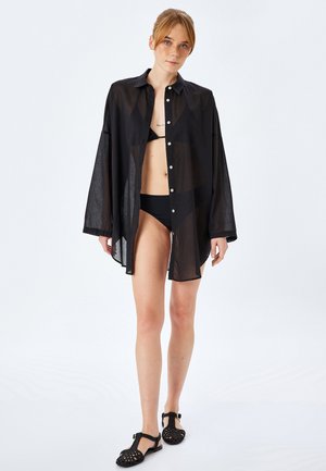 Zwarte transparante overhemden met lange mouwen, gecombineerd met een zwarte bikini. Heeft een relaxte pasvorm en een subtiele glans in een lichtgewicht stof.