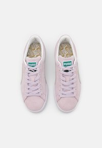 Baskets Puma en daim rose clair, avec des semelles blanches et des lacets blancs. Logo vert sur la languette. Motif d'intérieur de semelle doré texturé. Design minimaliste.