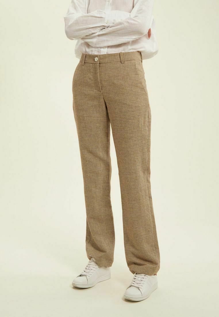 Pantalons à carreaux beige à coupe droite, avec une fermeture à bouton et des poches, associés à des baskets blanches et une chemise légère à manches longues.