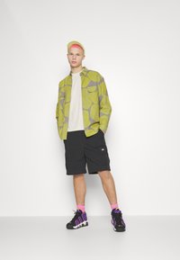 Green and gray patterned shirt over a white t-shirt, paired with dark cargo shorts and black sneakers featuring pink accents.