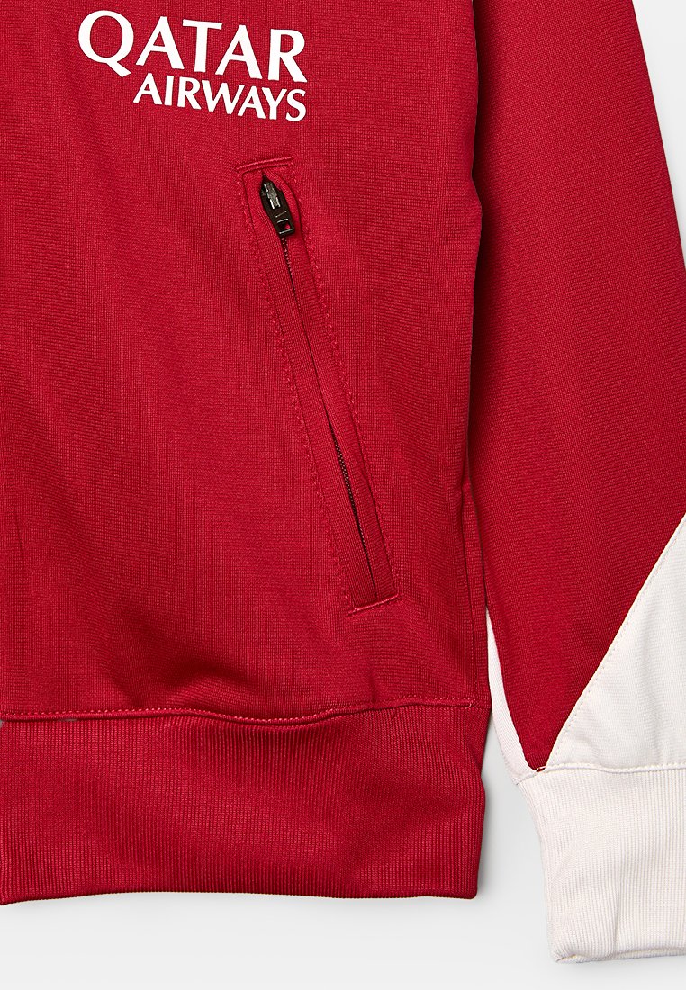 Veste rouge avec des accents de manches blanches, dotée d'une poche zippée et du logo "QATAR AIRWAYS" en blanc sur la poitrine. Tissu texturé.