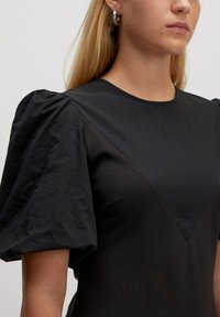 Zwarte jurk met puffmouwen, een ronde halslijn en een textiel met een V-vormige detail op het lijfje.