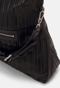 Czarna skórzana torebka o pionowej żebrowanej strukturze, z boczną kieszenią na zamek błyskawiczny oraz regulowanym paskiem z srebrnymi akcentami.
