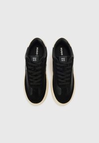 Ténis pretos com uma combinação de couro liso e camurça. Cadarços pretos, logótipo na língua e sola de borracha bege.