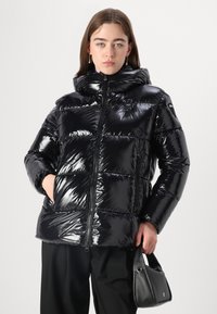 Chaqueta acolchada negra con un acabado brillante, cierre de cremallera y capucha. Presenta secciones acolchadas en horizontal y bolsillos laterales.
