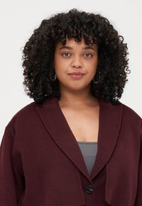 Burgundy wool coat with a large collar, single black button closure, and oversized fit. Fine texture and soft drape.