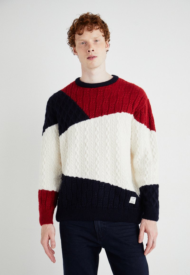 Jersey de punto con un diseño en bloques de color en rojo, azul marino y crema, con textura de trenzado. Los puños y el cuello acanalados mejoran la estructura.