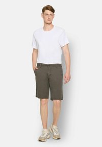 Shorts din bumbac de culoare verde închis, cu o croială dreaptă, buzunare frontale și închidere cu button, asortați cu un tricou simplu alb și adidași bej.