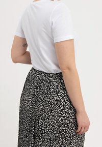 Vit bomulls t-shirt med kort ärm, parat med en svart kjol med ett vitt abstrakt mönster, veckad midja och flödande design.