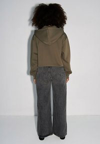 Przycięta oliwkowa bluza z kapturem na sznurku, w połączeniu z szerokimi, wyblakłymi czarnymi dżinsami z widocznym przeszyciem i tylnymi kieszeniami.