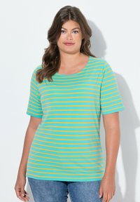 Camiseta de manga corta en verde azulado con rayas naranjas horizontales. Cuello redondo, corte relajado, tejido suave, combinada con jeans azules.