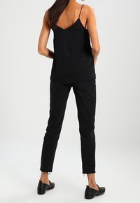 Svart ärmlös topp i mjuk tyg med tunna axelband, kombinerad med svarta slim-fit jeans med fransade nederkanter och svarta platta skor.