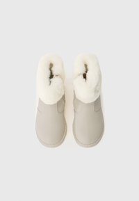 Beiga anklarboots med en mjuk, vit, pälsfodrad krage. Slät, strukturerad ovandel med elastiska sidopaneler och sydda souldetaljer.