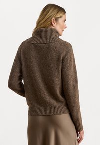 Hnedý pletený sveter s vysokým ribovaným golierom, textúrovanou tkaninou, spustenými ramenami a ribovaným lemom, nosený cez hladkú béžovú sukňu.