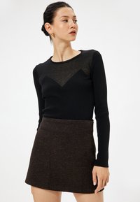 Zwarte geribbelde langemouwen top met een sheer chevrondesign op de borst, gecombineerd met een gestructureerde bruine minirok.